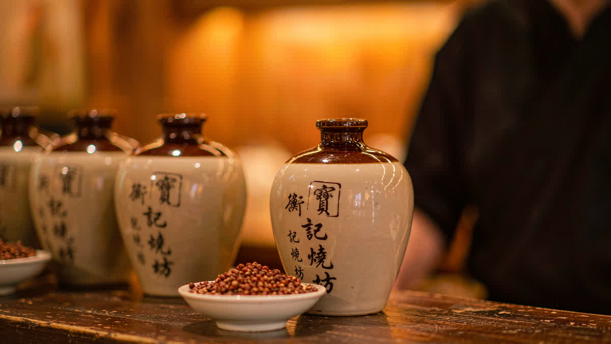 Traditional ceramic baijiu jars and sorghum grain on a rustic wooden table