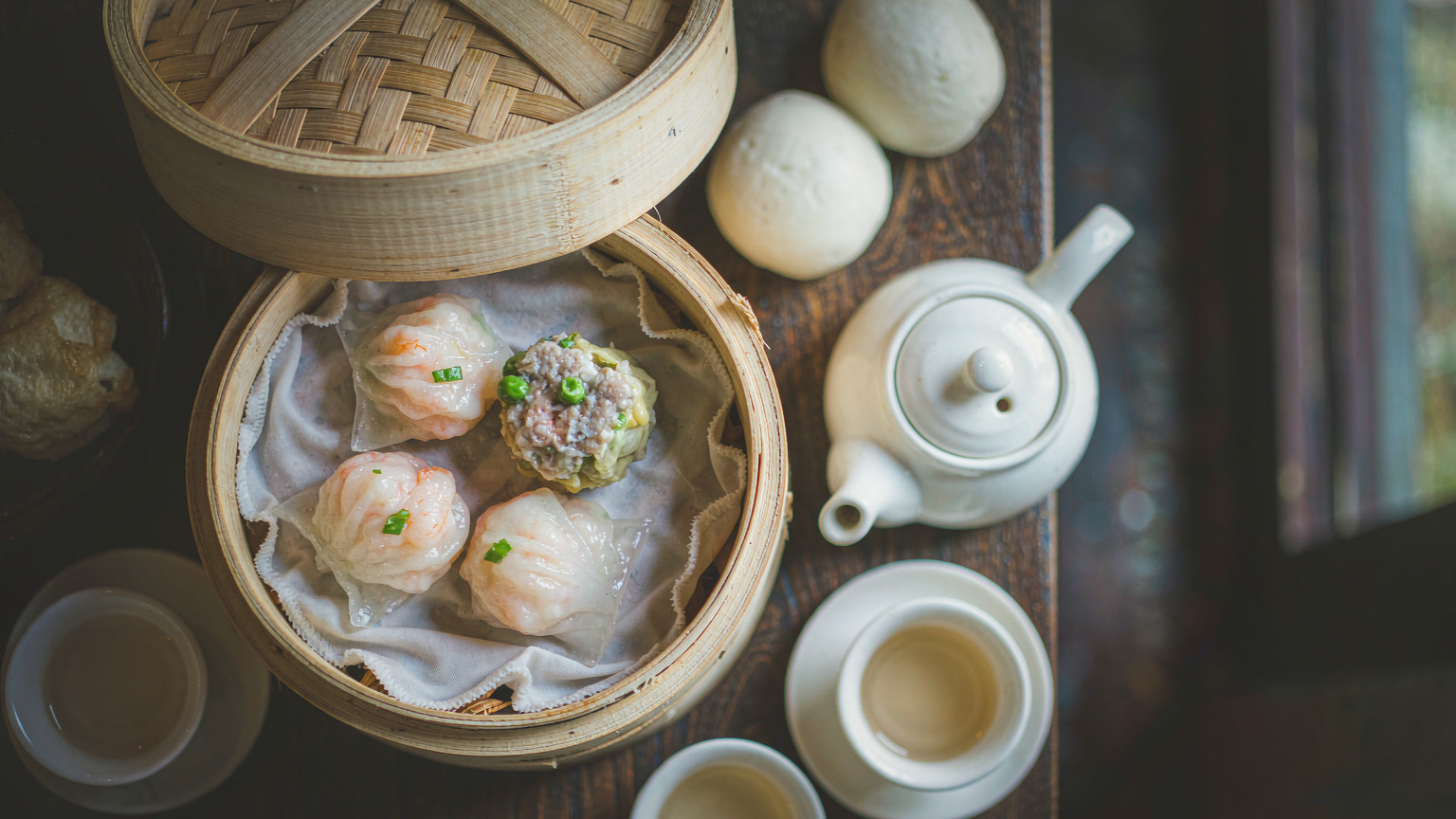 Bamboo steamer baskets of Cantonese dim sum with har gow and siu mai on a wooden restaurant table