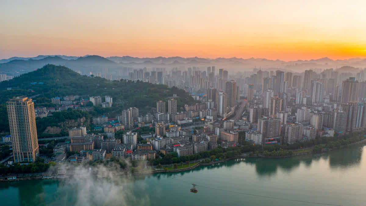 Chongqing at dusk with high-rise buildings climbing steep hillsides and a cable car crossing the river