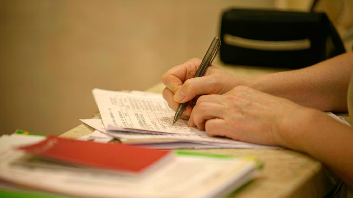 A customer's hands filling out a printed form with a pen at a Chinese bank service counter.
