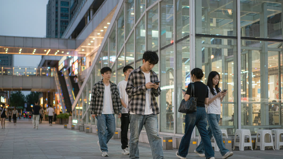 Young people walking on a modern Chinese shopping street at night while using smartphones