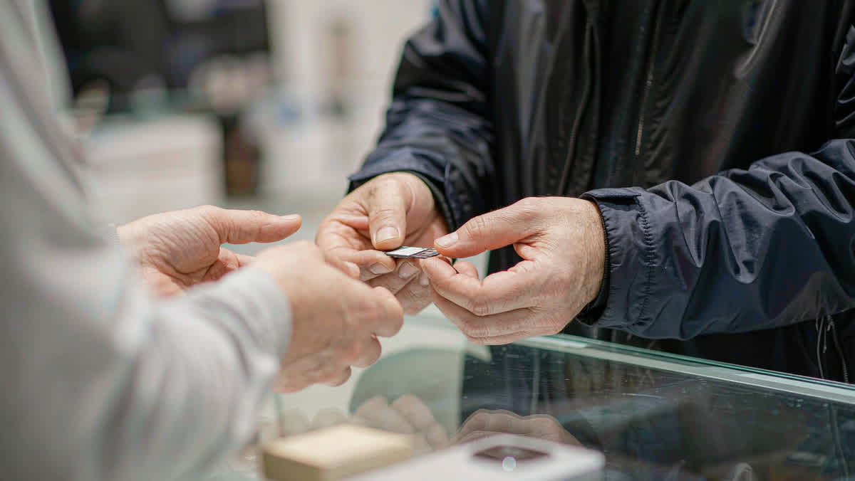 A pair of hands receiving a SIM card tray across a glass telecom store counter.
