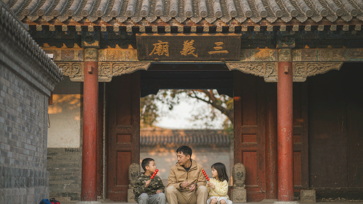 Two young children resting on stone steps outside a traditional Chinese temple gate during a family trip in China