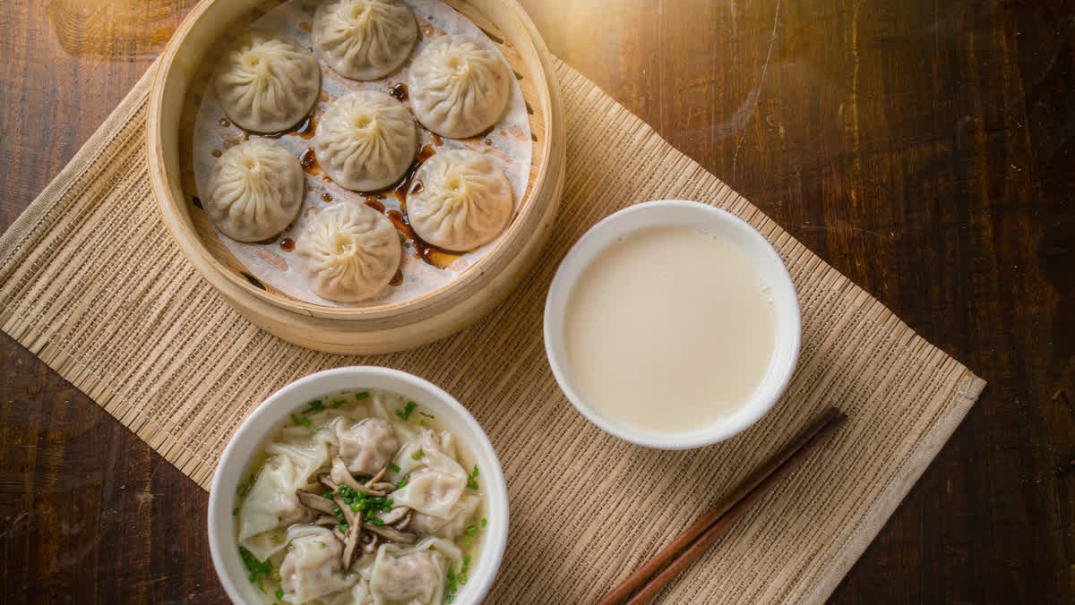 Traditional Chinese breakfast: xiaolongbao in a bamboo steamer served with soy milk and wonton soup