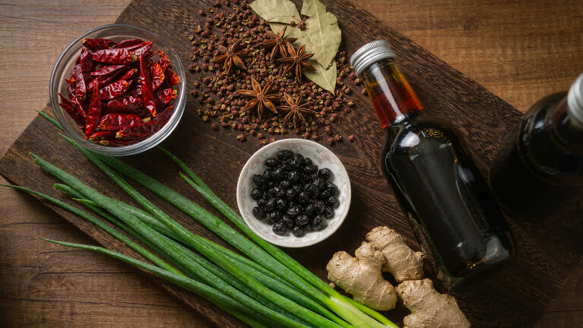 Flat-lay of Chinese cooking aromatics: dried chilies, Sichuan peppercorns, star anise, fermented black beans, scallions, ginger and soy sauce