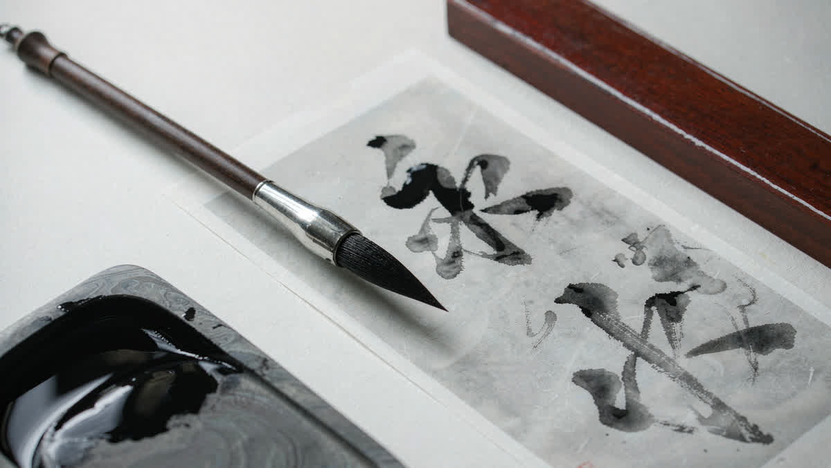 Chinese calligraphy strokes brushed onto rice paper beside an inkstone