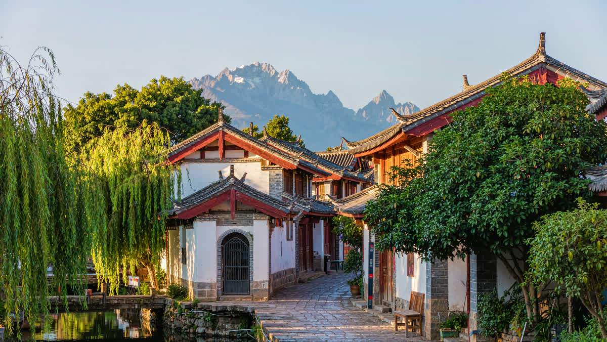 An old town alley in Yunnan with white walls, red-tiled roofs, a canal and blue mountains