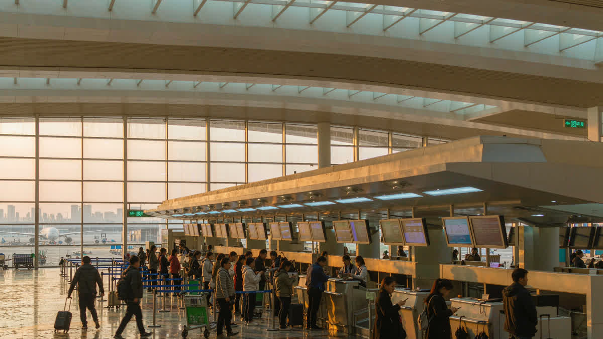 Early-morning check-in hall of a modern Chinese airport terminal, travellers queueing with suitcases and a jet visible through the windows