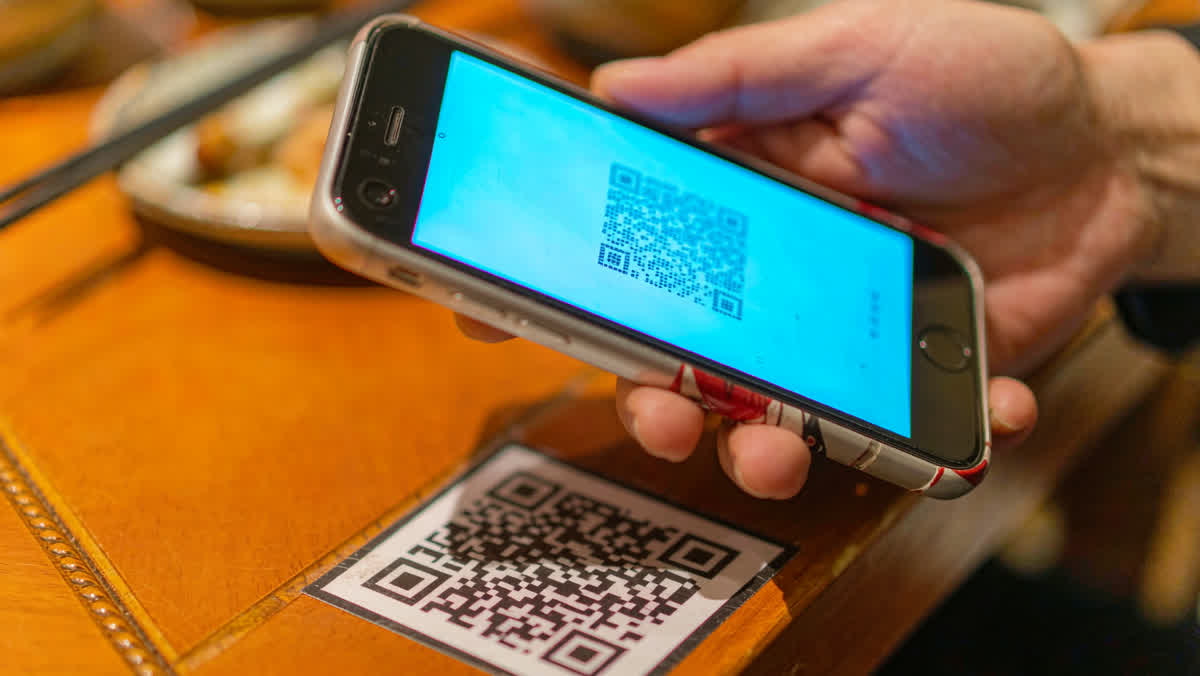 A smartphone scanning a printed QR code on a small wooden restaurant table.
