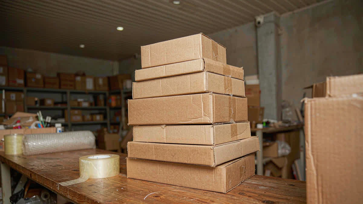 A neat stack of brown cardboard parcels of varying sizes on a wooden workbench at a shipping shop.
