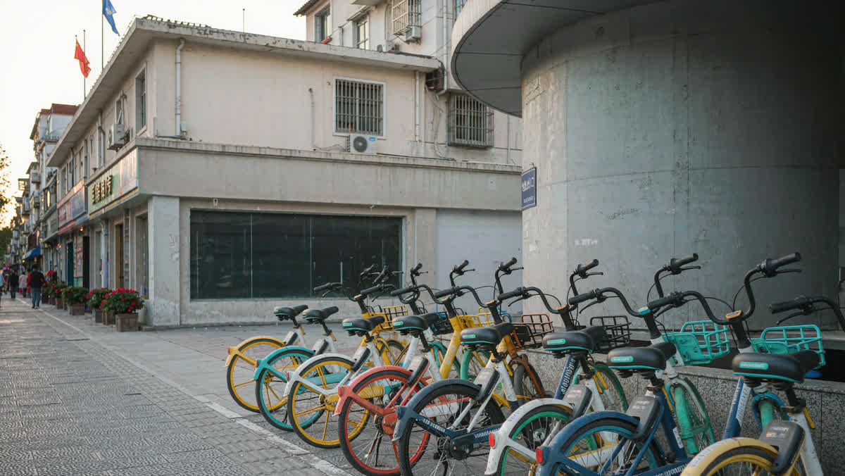 Rows of colorful shared bicycles parked on a sidewalk next to a subway entrance at evening