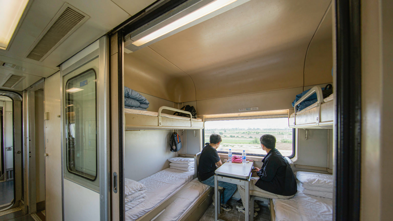 A modern Chinese EMU soft sleeper compartment with lower berths used as seating and bedding stowed on the upper bunks