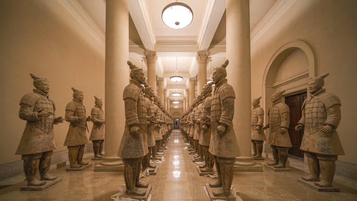 Long rows of terracotta warrior statues inside a large exhibition hall