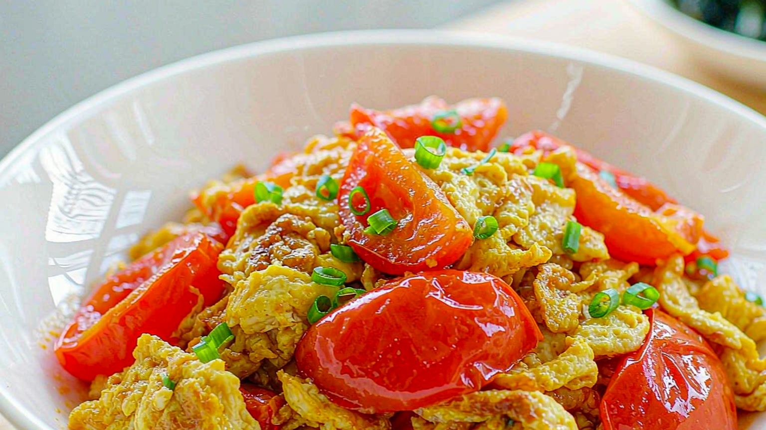 Bowl of Chinese tomato and egg stir-fry with scrambled egg and sliced scallion