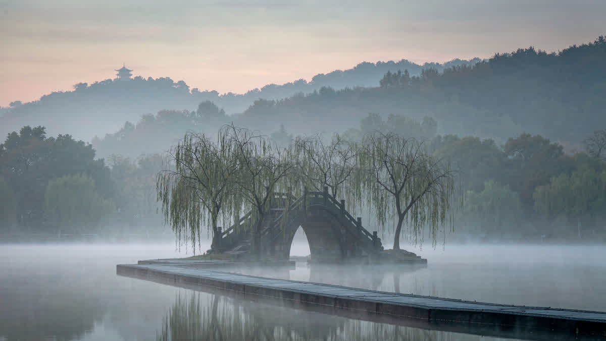 A stone arch bridge on the willow causeway at West Lake, Hangzhou, in early-morning mist